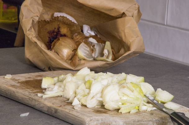 Нарезанный лук на доске и пилинги в коричневом пакете для переработки продуктов питания. - Фото, изображение