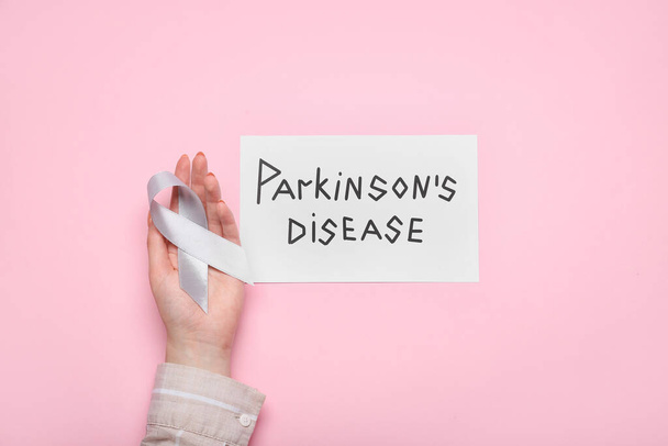 Papier met tekst PARKINSON 'S DISEASE, vrouwelijke hand en bewustzijnslint op roze achtergrond - Foto, afbeelding