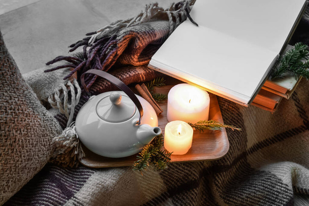 Teekanne, brennende Kerzen und aufgeschlagenes Buch auf Karo - Foto, Bild