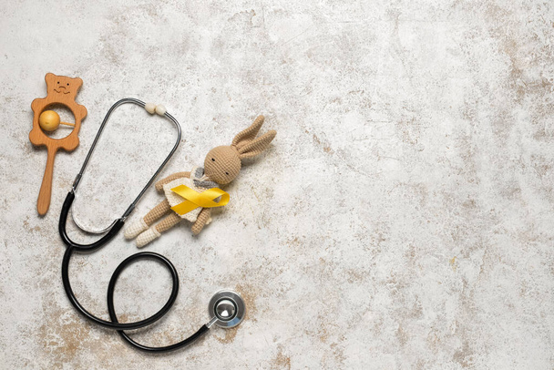 Іграшковий кролик із золотою стрічкою обізнаності, стукіт і стетоскоп на тлі гранджу. Міжнародний день раку дитячого віку - Фото, зображення