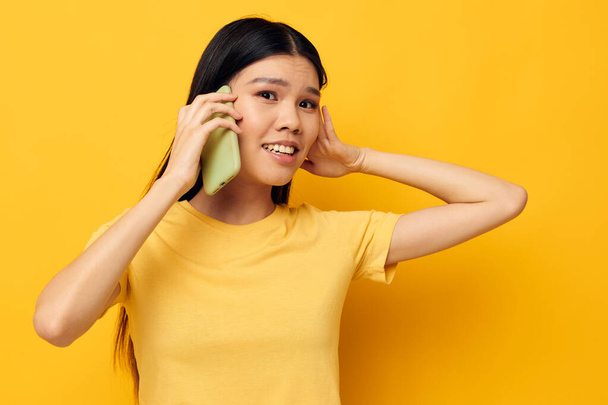 bonita morena hablando por teléfono posando tecnología amarillo fondo inalterado - Foto, Imagen