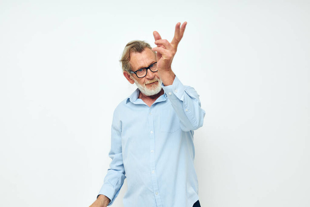 Portrait of happy senior man in blue shirts gestures with his hands light background - Foto, Imagem