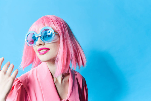 όμορφη γυναίκα με μπλε γυαλιά φοράει μια ροζ περούκα απομονωμένη φόντο - Φωτογραφία, εικόνα
