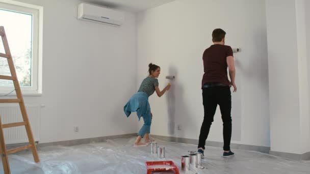 Joven pareja caucásica pintando la forma de la casa en la pared en casa nueva. Fotografía con cámara de helio RED en 8K  - Metraje, vídeo