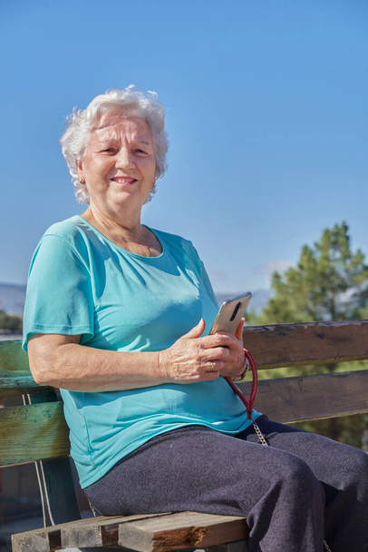 Ηλικιωμένη χαμογελαστή γυναίκα που χρησιμοποιεί smartphone στον πάγκο - Φωτογραφία, εικόνα