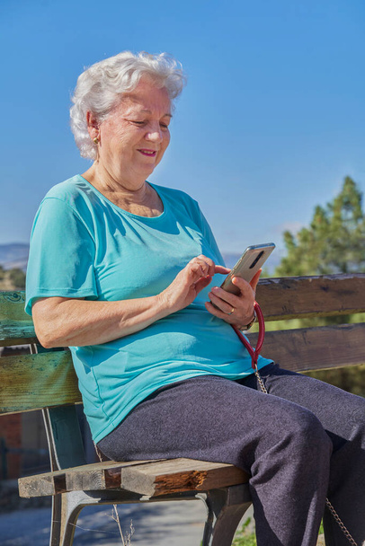 Senior woman messaging on smartphone on bench - Foto, Bild