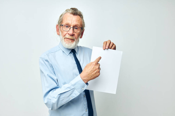 Senior grey-haired man holding documents with a sheet of paper light background - Foto, afbeelding
