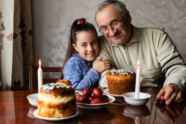 Счастливый пожилой человек дедушка готовится к Пасхе с внучкой. окрашенные цветные яйца на Пасху - Фото, изображение