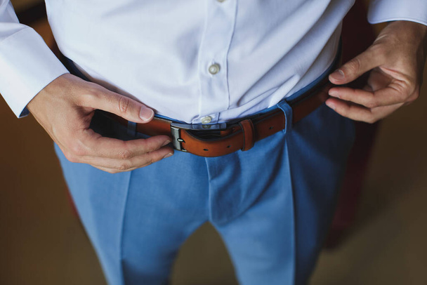 Man corrects belt, fees groom, mans hands, dressing, man buttons pants, jeans. - 写真・画像
