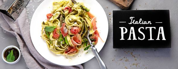 Těstoviny s chřestem a prosciutto na šedém pozadí. Tradiční italská koncepce potravin. Pohled shora, plochá plocha, panorama  - Fotografie, Obrázek