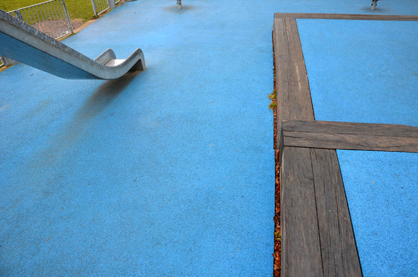 playground com corrediça de aço inoxidável, superfície de borracha azul. terraços pisados limitado por feixes maciços. Esgrima galvanizada com um portão contra cães. baloiços vermelhos em aço mola jardim berçário plástico - Foto, Imagem