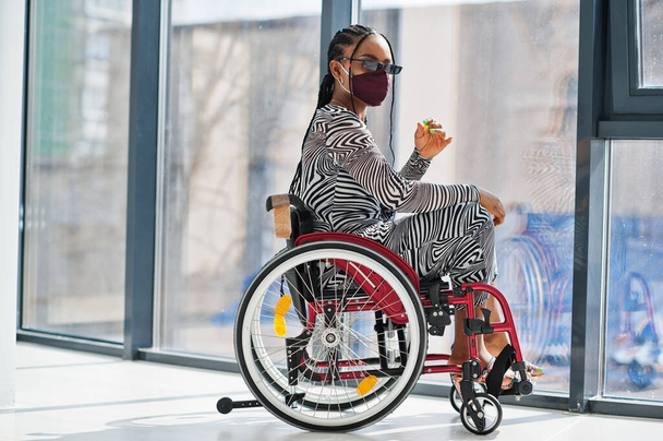 Young disabled African American woman in wheelchair at home, wear face mask. - Foto, imagen