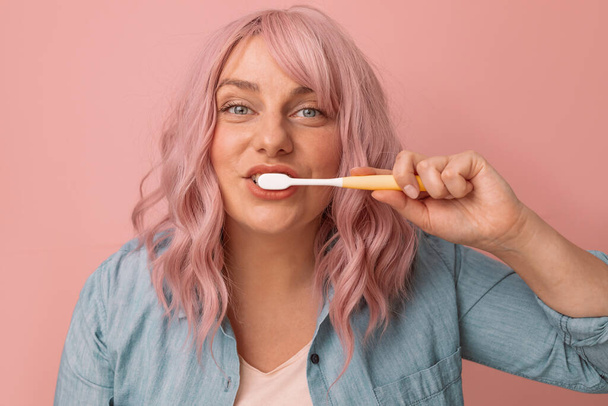 Gelukkig glimlachende vrouw poetsen gezonde tanden met tandenborstel op roze achtergrond Hygiëne concept - Foto, afbeelding
