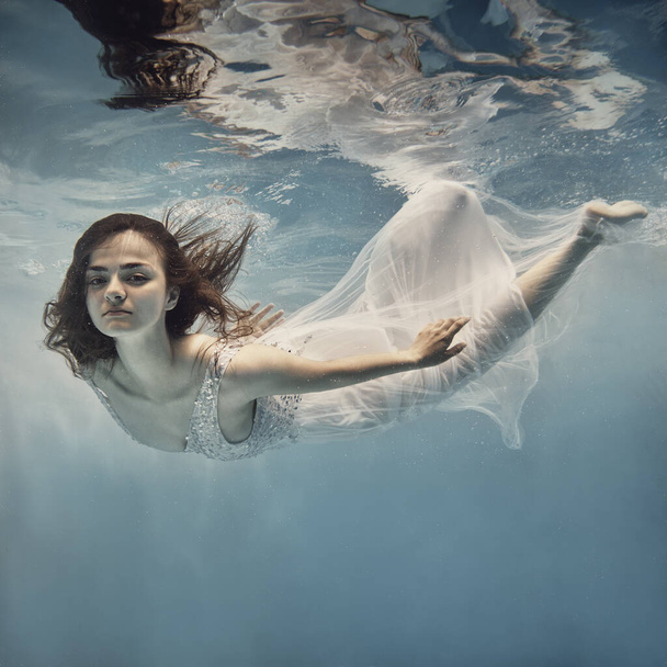      A girl in a white dress with dark hair swims underwater as if flying                           - Photo, image