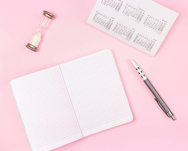 notepad, calendar, pen and hourglass on a pink background. View from above - Photo, image