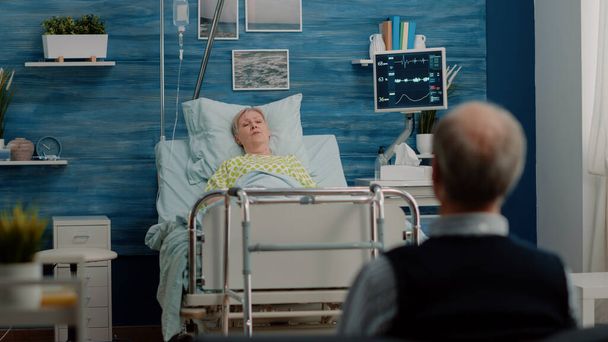 Alte Frau mit Krankheit ruht im Bett, während sie mit Ehemann spricht - Foto, Bild