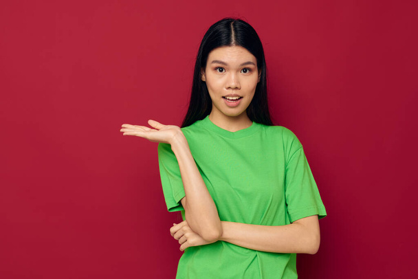 Charming young Asian woman green t-shirt gestures with his hands red background unaltered - Valokuva, kuva
