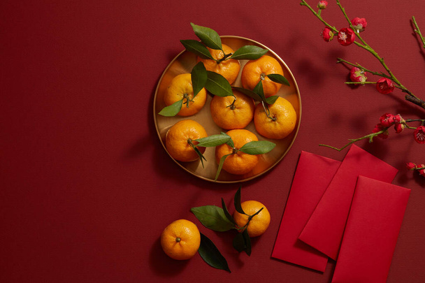 Κινέζικο σεληνιακό νέο έτος με μανταρίνι πορτοκαλί, λουλούδι και κόκκινη τσέπη σε κόκκινο φόντο, φωτογραφία περιεχομένου διακοπών Tet, top view - Φωτογραφία, εικόνα