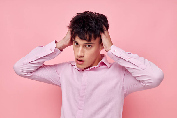 A young man in a pink shirt gesturing with his hands pink background unaltered - Фото, изображение