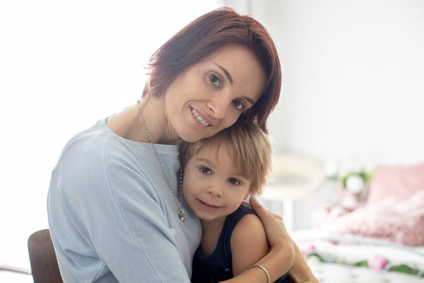 Portrait of mother and child, hugging on a back lit white background, enjoying family time together - Zdjęcie, obraz