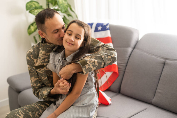 幸せなアメリカの家族の父親の肖像軍の制服とかわいい女の子の娘とともに米国の国旗カメラで抱き合って笑顔 - 写真・画像