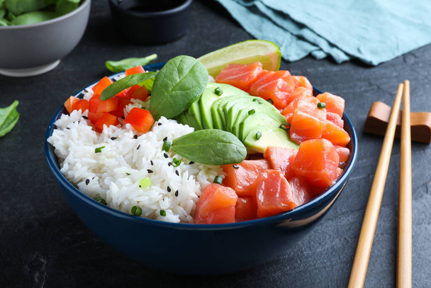 Delicious poke bowl with salmon, spinach and avocado served on black table - Photo, Image