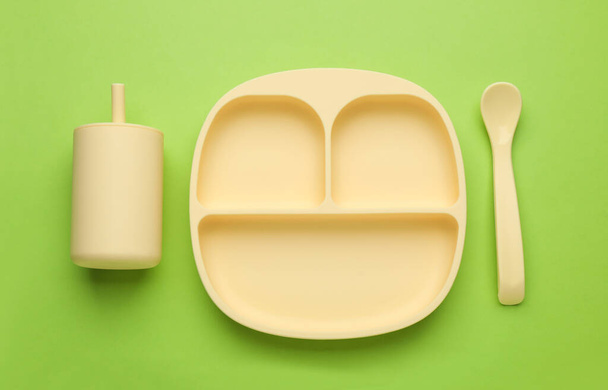 Set of plastic dishware on light green background, flat lay. Serving baby food - Foto, afbeelding