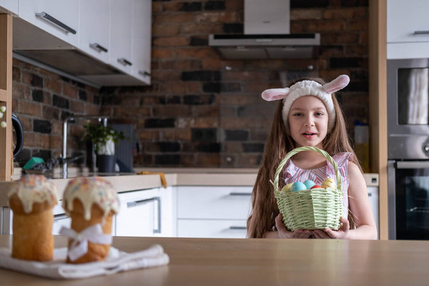 Piękne dziecko w bandażu z króliczymi uszami, z kolorowymi jajkami w koszyku, w domu w kuchni. Przygotowanie do Wielkanocy - Zdjęcie, obraz