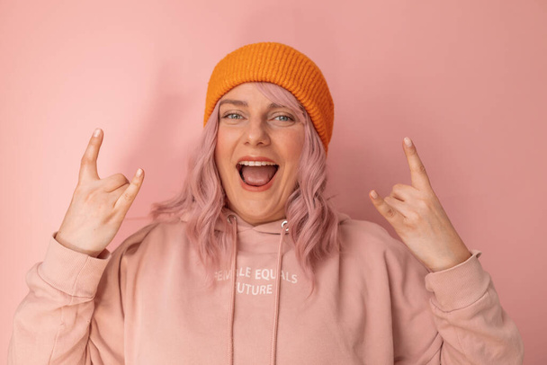 Portrait de funky fou souriant 20s femme montrant rock n roll signe isolé sur fond de couleur rose - Photo, image