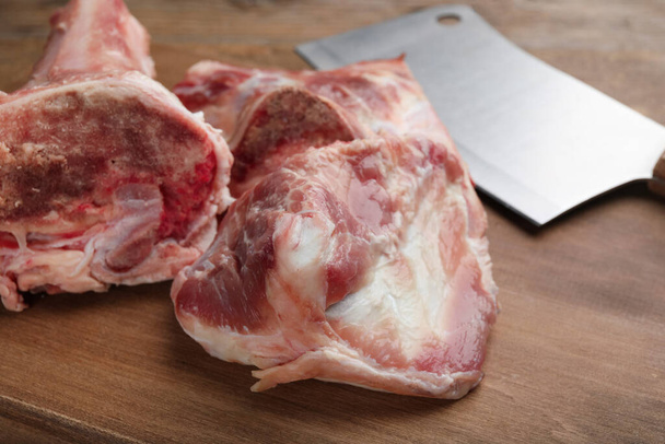 Cutting board with raw chopped meaty bones and butcher knife on wooden table, closeup - Foto, Imagem