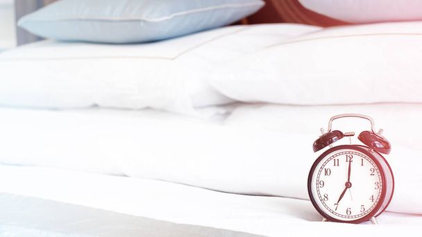 Reloj despertador de metal negro borroso que muestra a las 7 de la mañana en una cama con sábanas blancas con espacio para copiar. Temprano por la mañana despierta, correcta rutina diaria.  - Foto, imagen