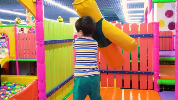 Um menino pré-escolar de 4 anos brinca com um saco de perfuração para boxe na sala de jogos, um centro de entretenimento para crianças - Filmagem, Vídeo