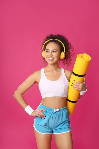 Beautiful African American woman with yoga mat and headphones on pink background - Fotografie, Obrázek