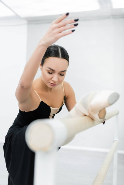 young ballerina stretching at barre in studio on blurred foreground - Photo, Image