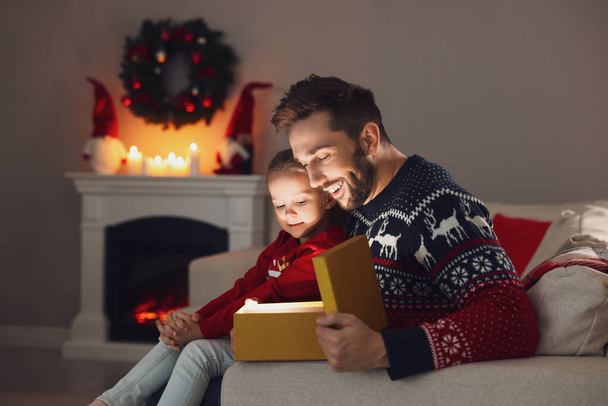 Father and his cute daughter opening gift box with magical light at home. Christmas celebration - Foto, imagen