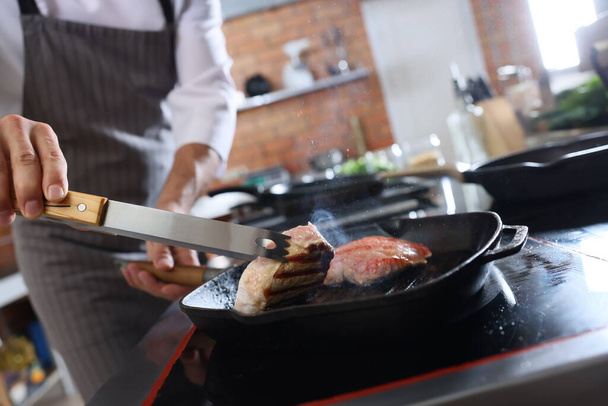 Профессиональный повар готовит мясо на плите на кухне ресторана, крупный план - Фото, изображение