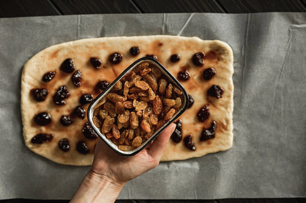 Baking sweet cottage cheese braided bread with raisins and jam. Rolled out dough with jam on the parchment paper, a close-up of a bowl of raisins. Overhead shot. - Fotografie, Obrázek