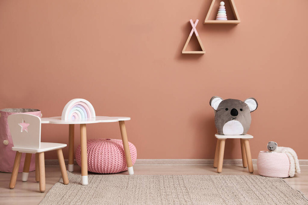 Leuke kinderkamer interieur met meubels, speelgoed en wigwam vormige planken op roze muur - Foto, afbeelding