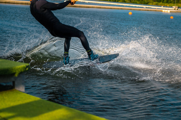 Wakeboarder cutting water with edge of board creating splashes while starting off dock - Photo, Image