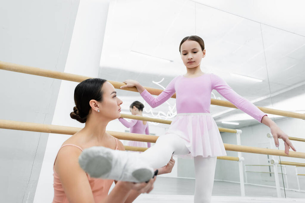 Genç dans öğretmeni bale okulunda kızın bacağını tutuyor. - Fotoğraf, Görsel
