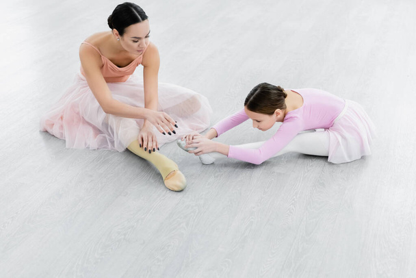 preteen girl stretching on floor near young ballet master in dance studio - Photo, Image