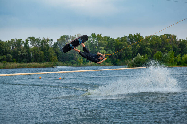 Tapasztalt wakeboard lovas ugrás és forgó levegőben tartja a vontató kábel - Fotó, kép