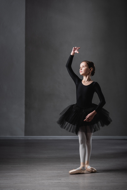 vue pleine longueur de fille en tutu noir pratiquant des éléments chorégraphiques en studio de ballet - Photo, image