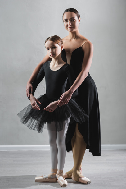 vista completa del profesor de ballet y la niña en tutú mirando a la cámara durante el ensayo - Foto, imagen
