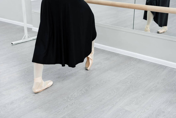 cropped view of ballerina in black dress training at barre in studio - Fotoğraf, Görsel