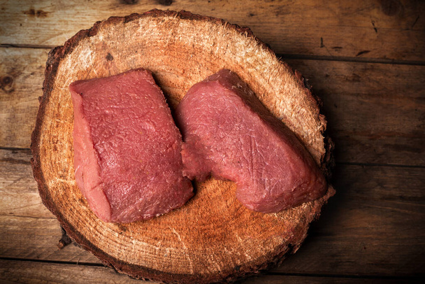 Top view of raw game meat, beef. Steaks, pieces of red meat on a wooden chopping block, wood slice, on vintage boards. High quality meat from roe deer, deer, fallow deer. - Photo, Image