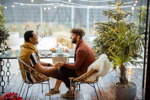 Dwóch wielorasowych mężczyzn rozmawiających ze sobą przy stole na podwórku - Zdjęcie, obraz