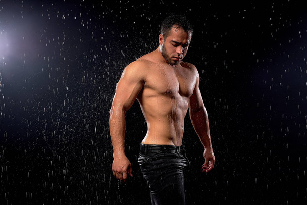 Side view on fit man bodybuilder posing at camera, standing in rain. Sporty muscular guy - Photo, Image