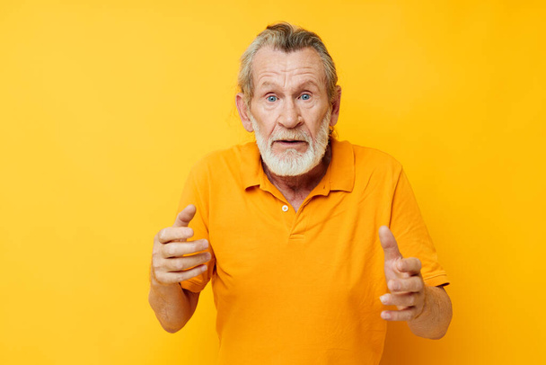 Senior grey-haired man with a gray beard emotion gestures hands yellow background - Foto, Bild