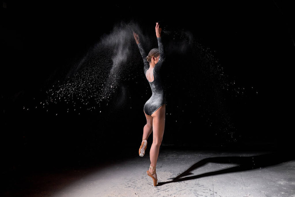 Flexible ballet dancer woman dancing and sprinkle flour on black background - Fotoğraf, Görsel